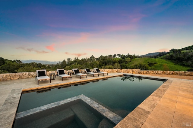 pool at dusk with a mountain view, a patio, and an in ground hot tub