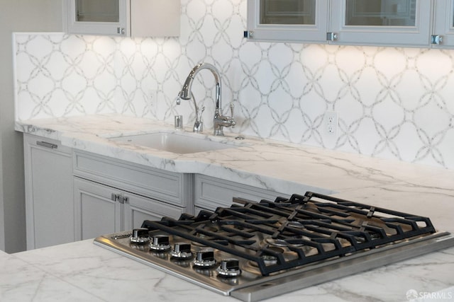 room details featuring stainless steel gas stovetop, decorative backsplash, light stone counters, and sink