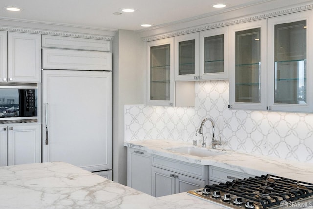 kitchen featuring light stone countertops, tasteful backsplash, sink, built in appliances, and white cabinets