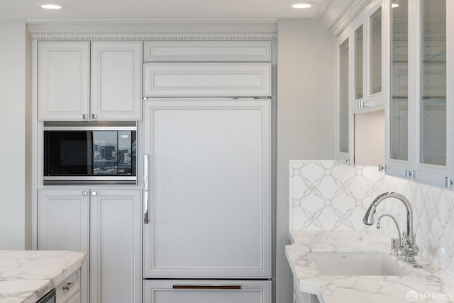 kitchen with light stone countertops, sink, white cabinetry, backsplash, and built in appliances