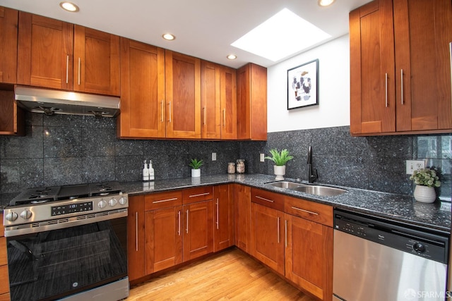 1579 46th Ave, San Francisco, CA 94122 - kitchen featuring appliances with stainless steel finishes, under cabinet range hood, brown cabinetry, a skylight, and dark stone countertops
