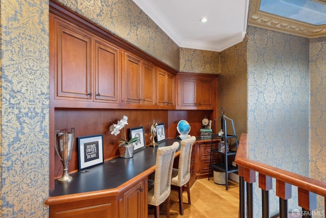 office area with built in desk, ornamental molding, light wood-style floors, and wallpapered walls