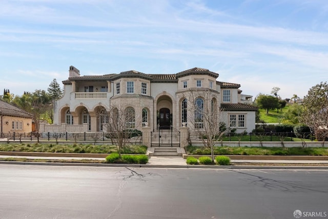 mediterranean / spanish-style home with a fenced front yard, stone siding, a gate, a balcony, and stucco siding