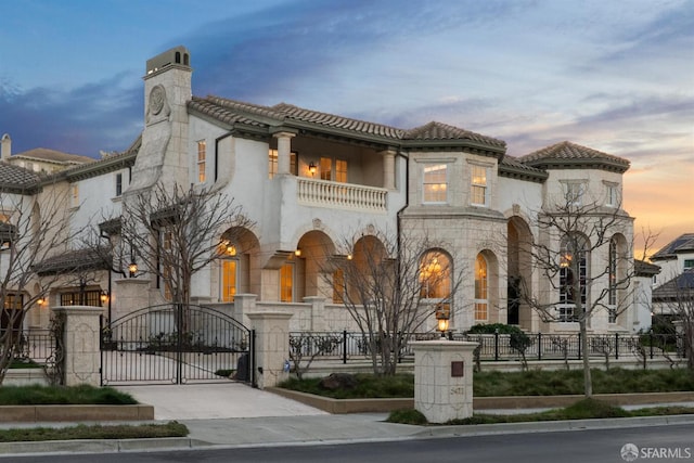 mediterranean / spanish-style home with a gate, a balcony, a fenced front yard, and stone siding
