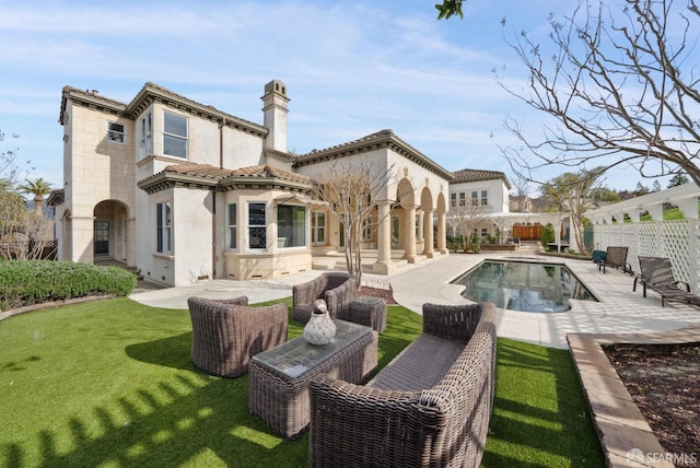 rear view of property with stucco siding, a patio, a chimney, and a tiled roof