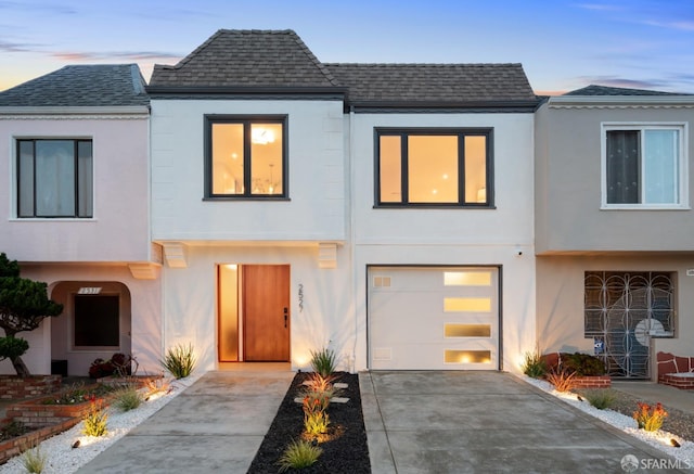 view of front of home featuring concrete driveway, roof with shingles, an attached garage, and stucco siding