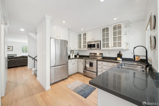 kitchen featuring stainless steel appliances, dark countertops, light wood-style floors, and a sink