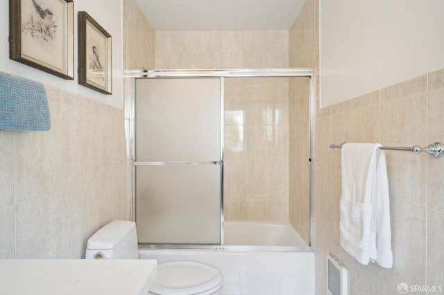 bathroom featuring visible vents, toilet, enclosed tub / shower combo, vanity, and tile walls