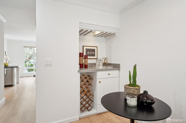 interior space with light wood-style flooring, baseboards, ornamental molding, dishwasher, and a bar