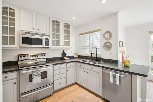 kitchen featuring dark countertops, light wood-style flooring, appliances with stainless steel finishes, white cabinetry, and a sink