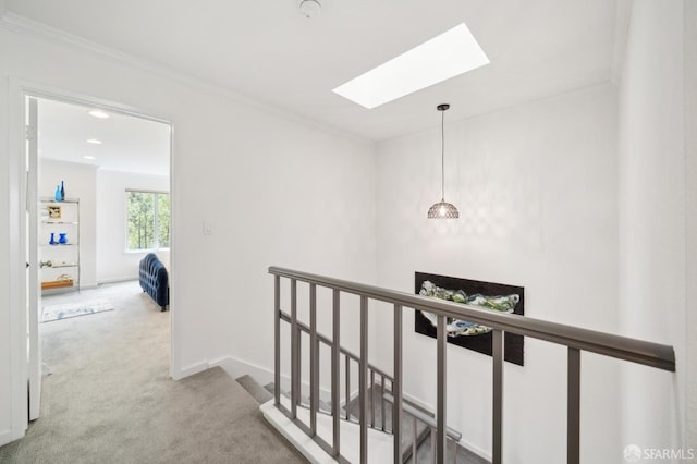 hall featuring a skylight, carpet, ornamental molding, an upstairs landing, and baseboards