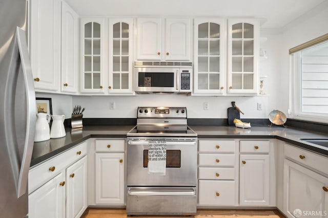 kitchen featuring stainless steel appliances, dark countertops, glass insert cabinets, and white cabinets