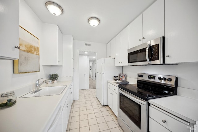 kitchen with appliances with stainless steel finishes, light tile patterned floors, white cabinetry, and sink