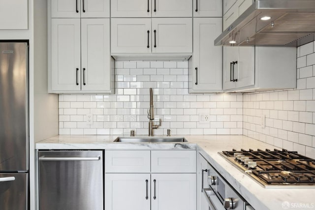 kitchen featuring sink, range hood, white cabinets, stainless steel appliances, and light stone countertops