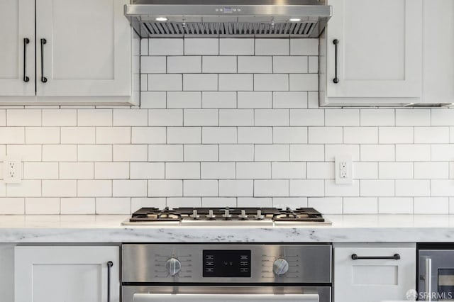 kitchen with white cabinets, appliances with stainless steel finishes, tasteful backsplash, and range hood