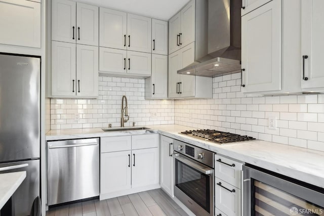 kitchen with tasteful backsplash, beverage cooler, white cabinetry, wall chimney exhaust hood, and appliances with stainless steel finishes