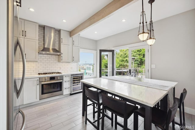 kitchen with wine cooler, light hardwood / wood-style floors, beam ceiling, wall chimney exhaust hood, and stainless steel appliances