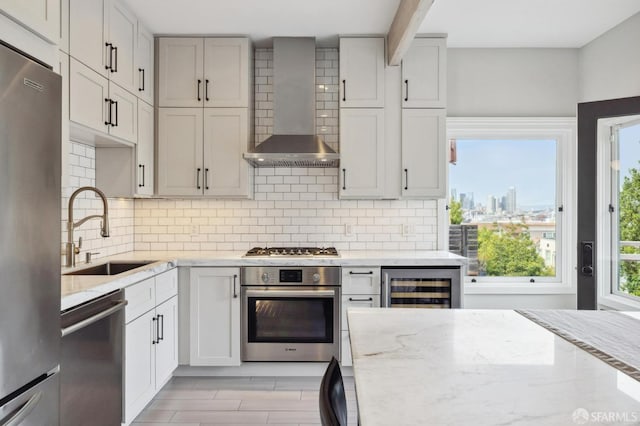 kitchen featuring light stone counters, wine cooler, sink, wall chimney range hood, and appliances with stainless steel finishes