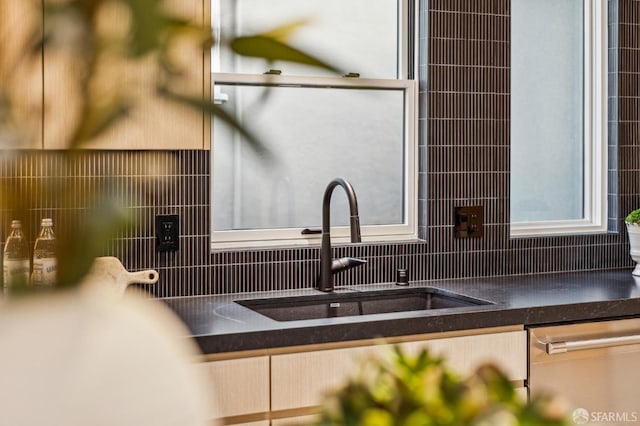 kitchen with dark countertops, stainless steel dishwasher, tasteful backsplash, and a sink