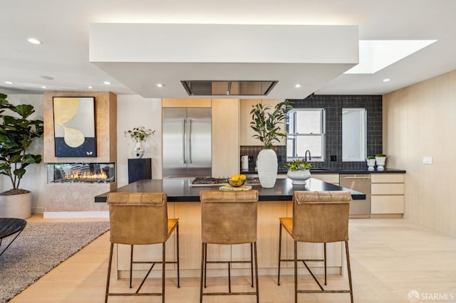 kitchen featuring dark countertops, appliances with stainless steel finishes, a center island, island exhaust hood, and a fireplace