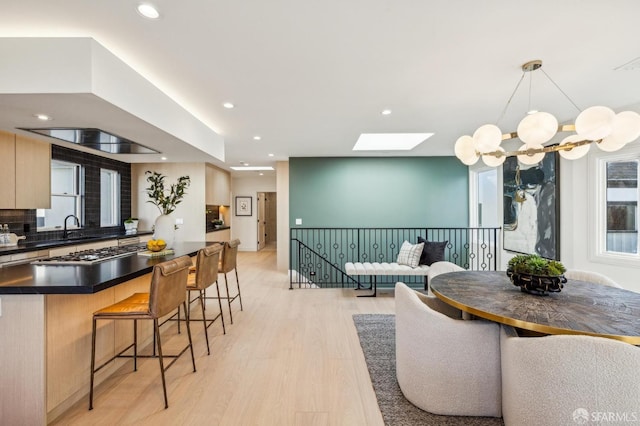 kitchen with stainless steel gas cooktop, a kitchen breakfast bar, open floor plan, light wood finished floors, and dark countertops