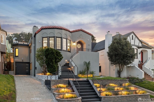 mediterranean / spanish home with a garage, a tile roof, stairway, decorative driveway, and stucco siding