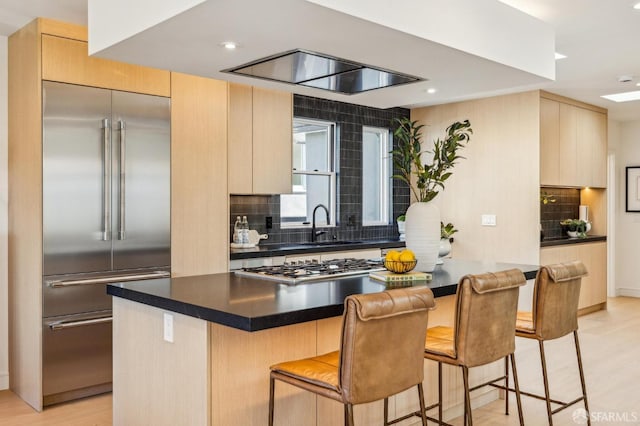 kitchen featuring stainless steel appliances, tasteful backsplash, a breakfast bar area, and light brown cabinetry