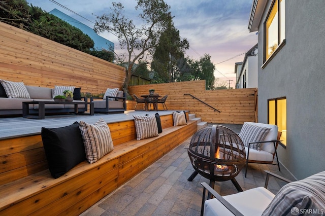 patio terrace at dusk with an outdoor living space with a fire pit and fence