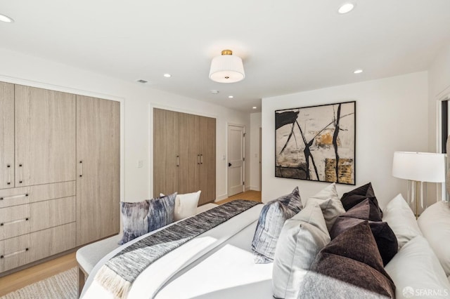 bedroom with recessed lighting, visible vents, light wood-style flooring, and two closets