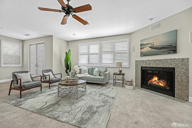 carpeted living room featuring ceiling fan, a fireplace, and a textured ceiling