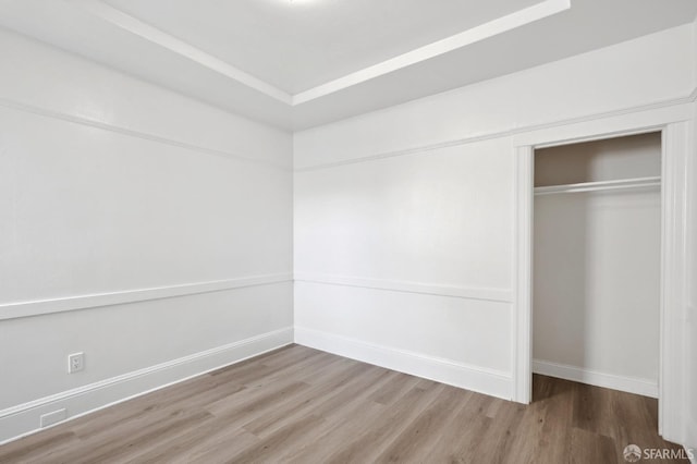unfurnished bedroom with a closet, a raised ceiling, baseboards, and wood finished floors