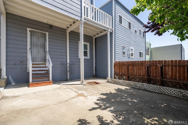 view of patio with fence, entry steps, and a balcony