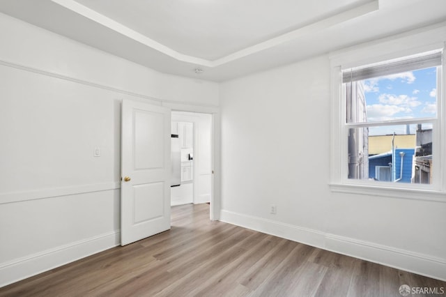 unfurnished room with a raised ceiling, baseboards, and wood finished floors