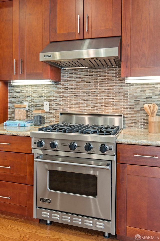 221 Noe St Unit 12, San Francisco, CA 94114 - kitchen with premium stove, wall chimney exhaust hood, light stone countertops, tasteful backsplash, and brown cabinets