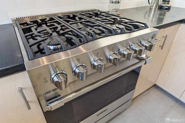 room details featuring high end stainless steel range oven, decorative backsplash, and light brown cabinetry