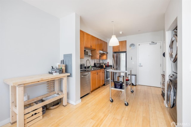 kitchen featuring light wood-type flooring, stacked washer and dryer, sink, appliances with stainless steel finishes, and decorative light fixtures