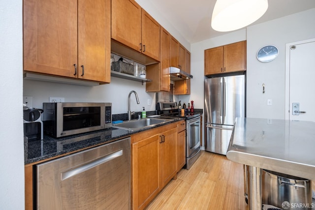 kitchen featuring appliances with stainless steel finishes, dark stone counters, sink, and light hardwood / wood-style flooring