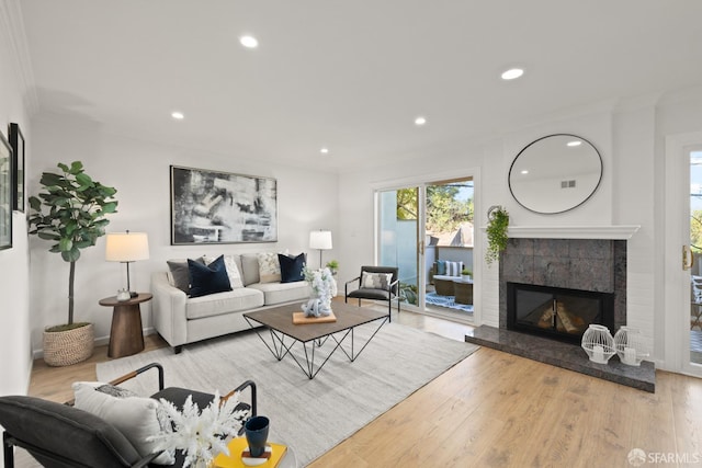 living area featuring visible vents, a tiled fireplace, wood finished floors, recessed lighting, and crown molding