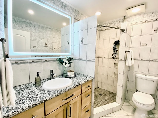 bathroom featuring toilet, vanity, a tile shower, tile patterned floors, and tile walls