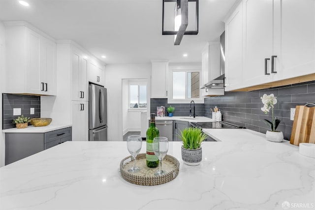 kitchen with white cabinets, decorative backsplash, light stone countertops, stainless steel appliances, and wall chimney range hood