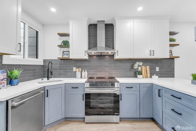 kitchen featuring stainless steel appliances, a sink, white cabinets, wall chimney range hood, and open shelves