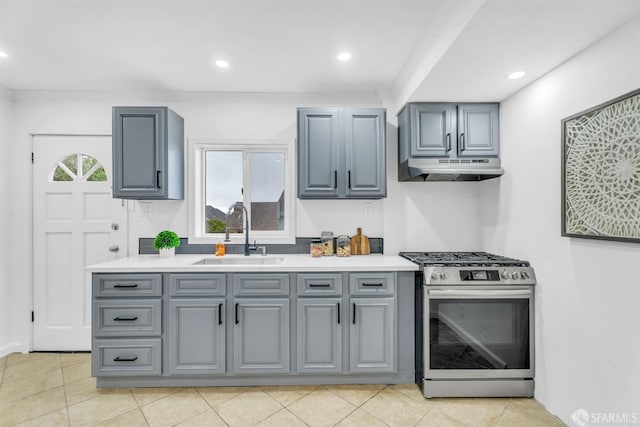 kitchen with stainless steel gas range, a sink, under cabinet range hood, and gray cabinetry