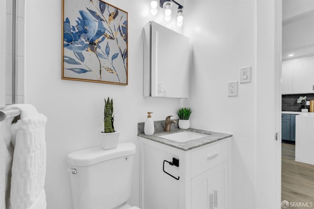 bathroom with toilet, decorative backsplash, wood finished floors, and vanity