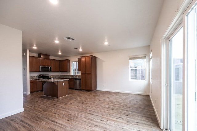 kitchen featuring light stone countertops, hardwood / wood-style floors, a breakfast bar, a kitchen island, and appliances with stainless steel finishes