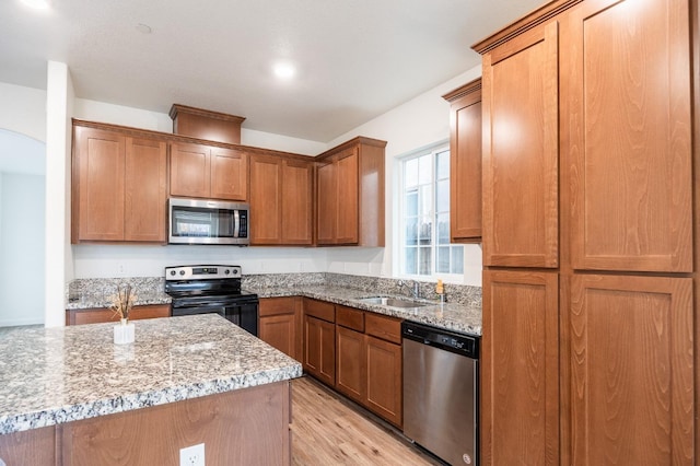 kitchen featuring light stone countertops, appliances with stainless steel finishes, light wood-type flooring, and sink