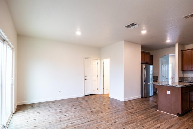 kitchen with wood-type flooring, stainless steel fridge, a center island, and dark stone countertops