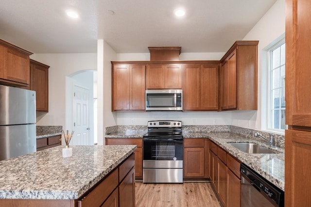 kitchen featuring light stone countertops, sink, stainless steel appliances, light hardwood / wood-style flooring, and a kitchen island