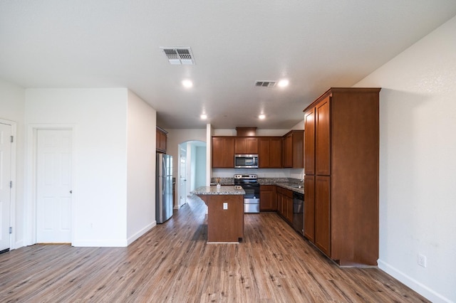 kitchen featuring light stone countertops, light wood-type flooring, appliances with stainless steel finishes, a kitchen island, and a breakfast bar area