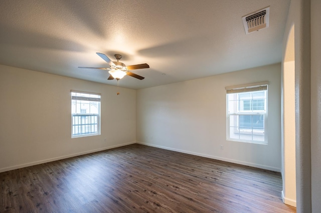 empty room featuring ceiling fan, dark wood-type flooring, and a wealth of natural light