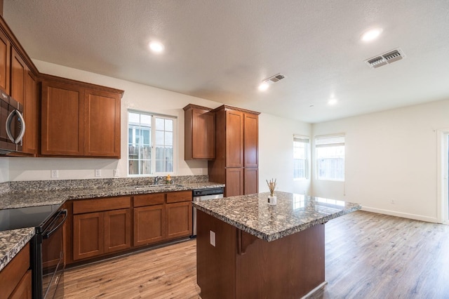 kitchen featuring dark stone countertops, sink, stainless steel appliances, and light hardwood / wood-style flooring